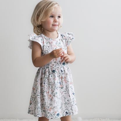 Girl standing in front of a white background, wearing Wildflower Flutter Dress, designed by Burrow and Be