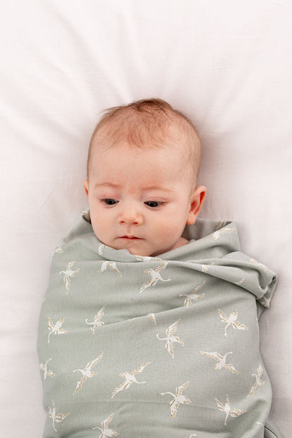 Baby wrapped in Swan Flight Swaddle Blanket by Burrow and Be - detail view