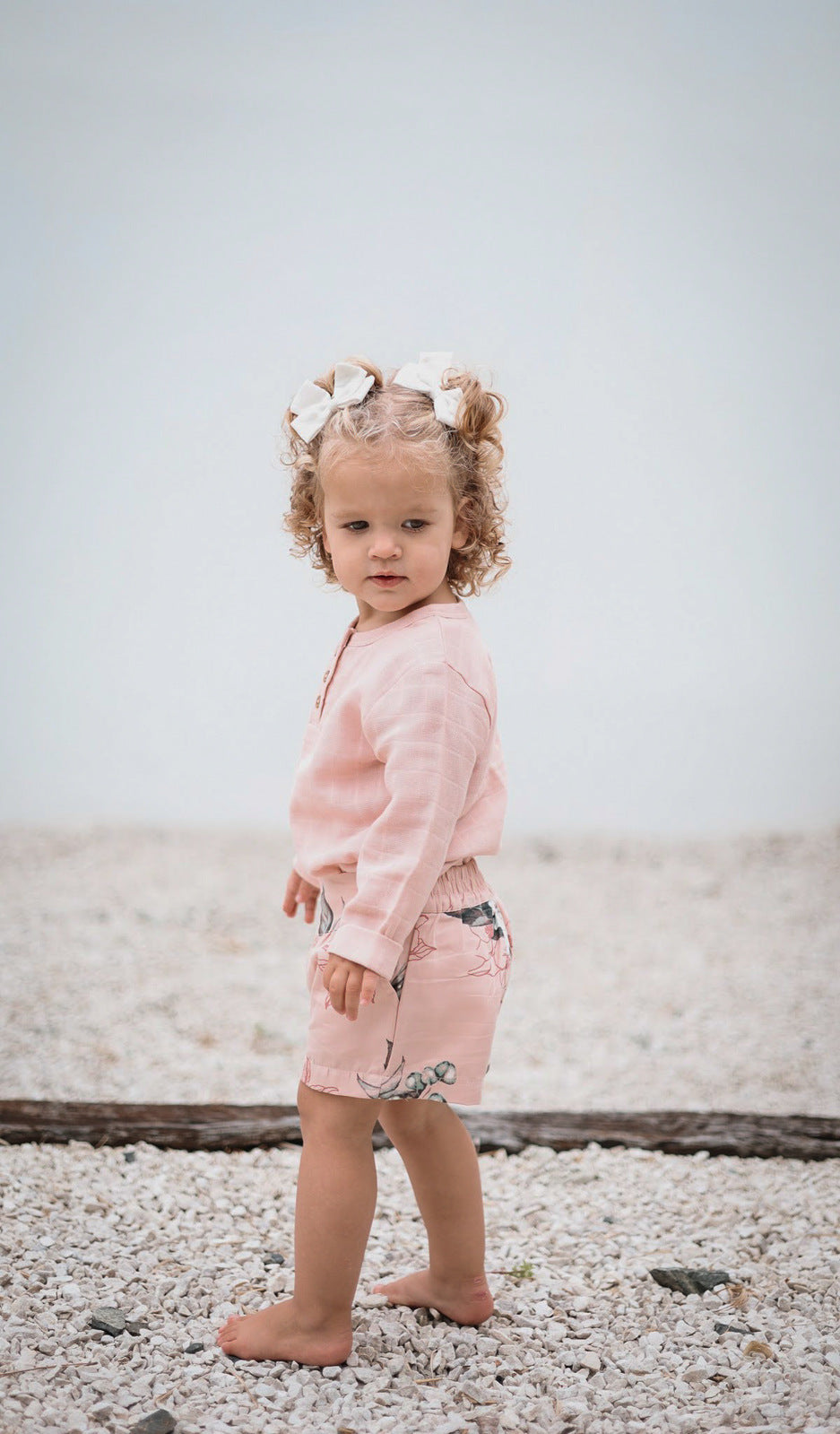Baby girl standing on the beach, wearing Burrow and Be Tropical Bouquet Lyla Shorts