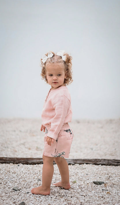 Baby girl standing on the beach, wearing Burrow and Be Tropical Bouquet Lyla Shorts