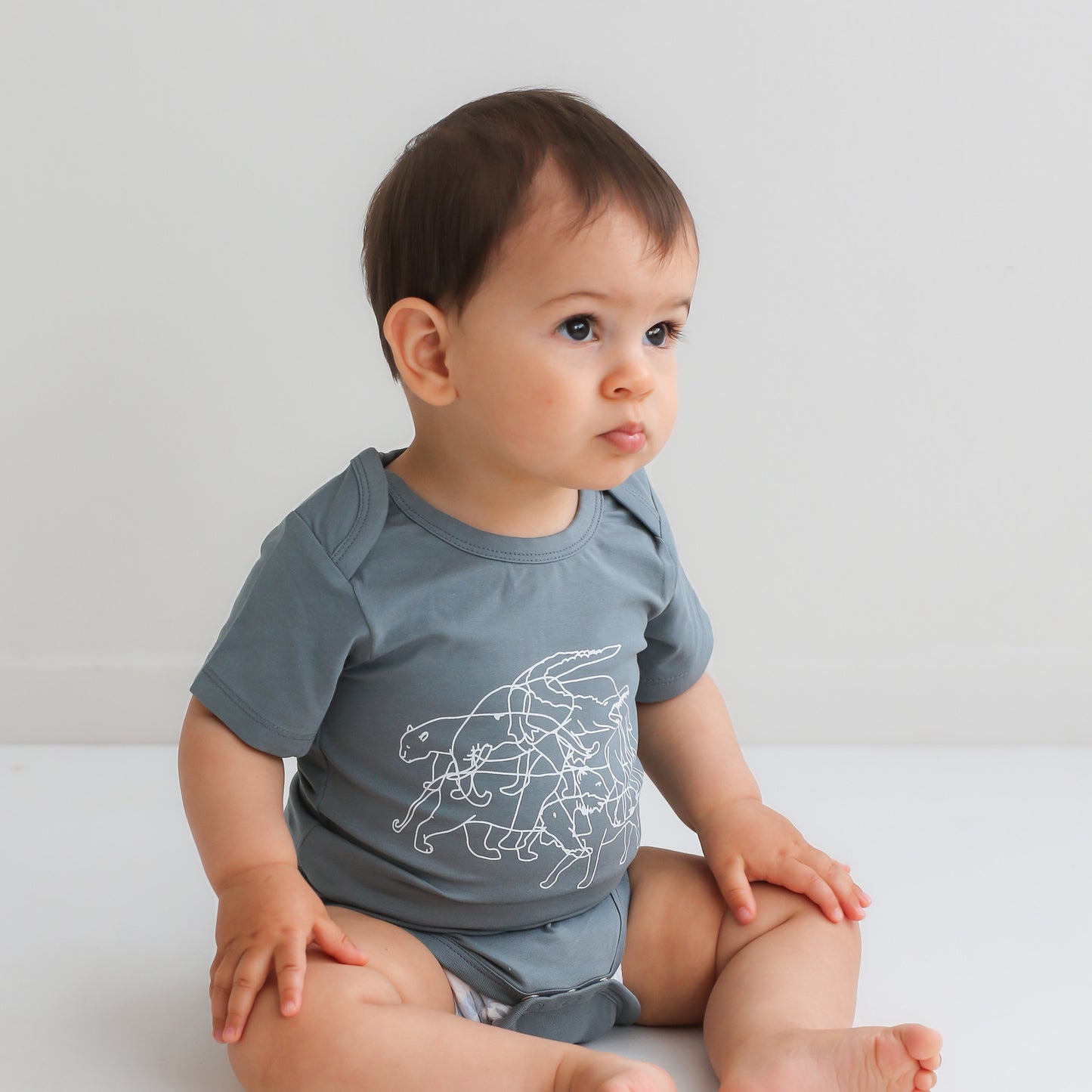 Baby boy sitting on a white floor against a white background wearing Lost on Storm Bodysuit, designed by Burrow and Be