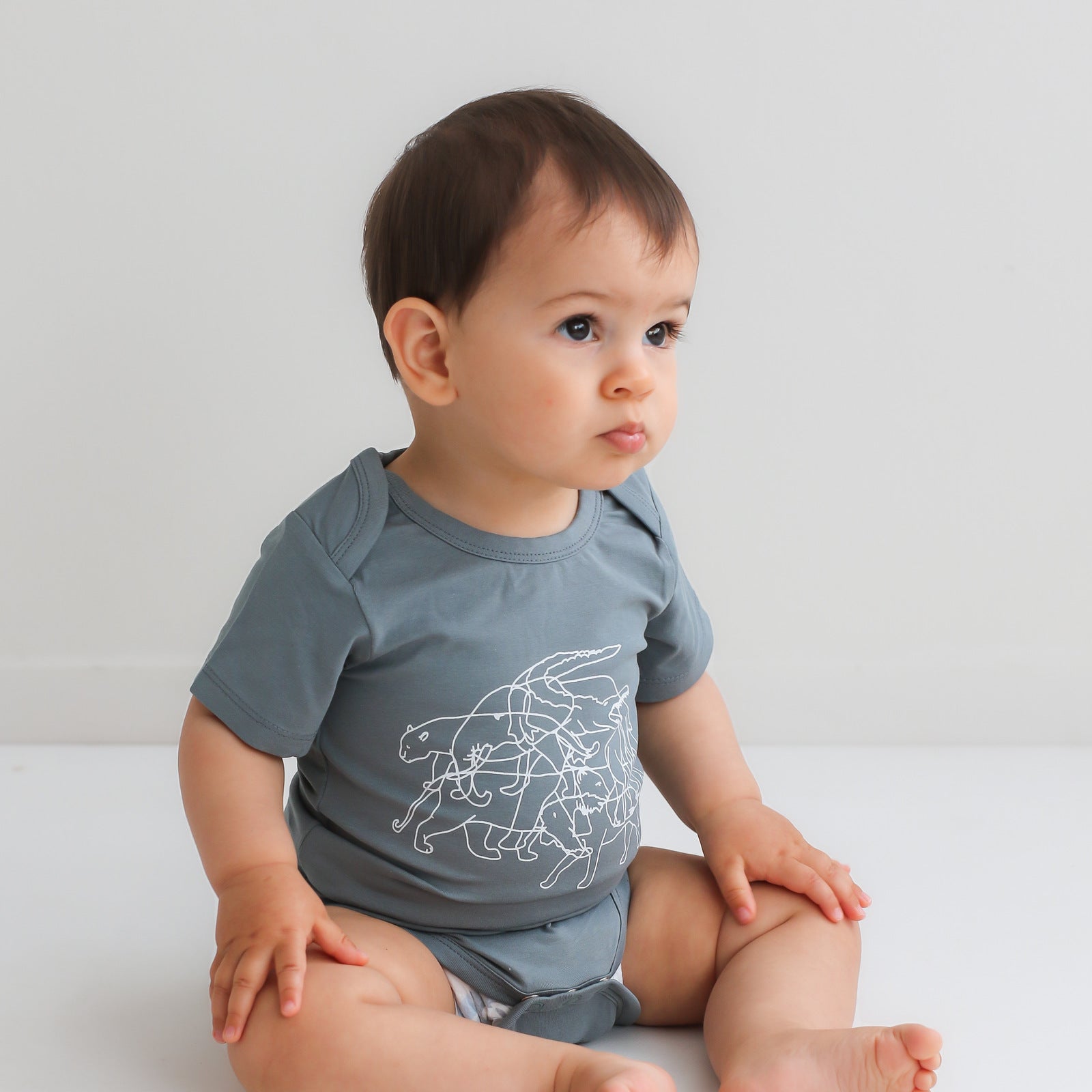 Baby boy sitting on a white floor against a white background wearing Lost on Storm Bodysuit, designed by Burrow and Be